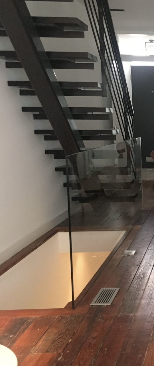 A glass panel rising out of the floor beside a floating staircase.