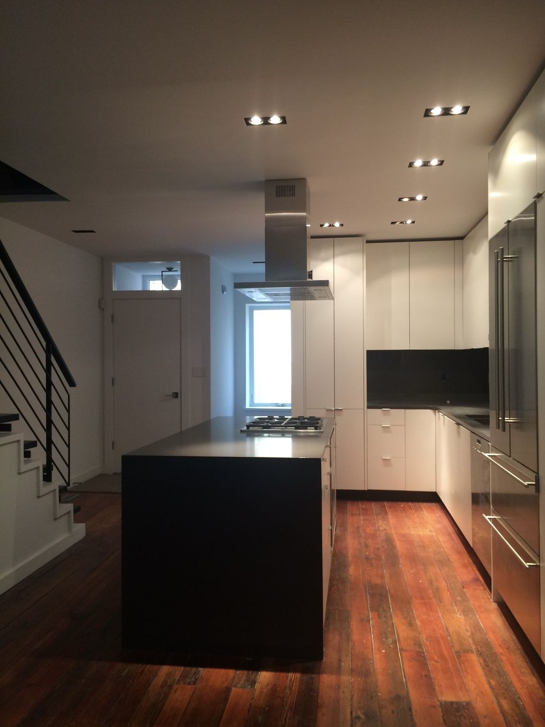Looking down the length of the kitchen past the island toward the tall refrigerator wall, with original pine floors.
